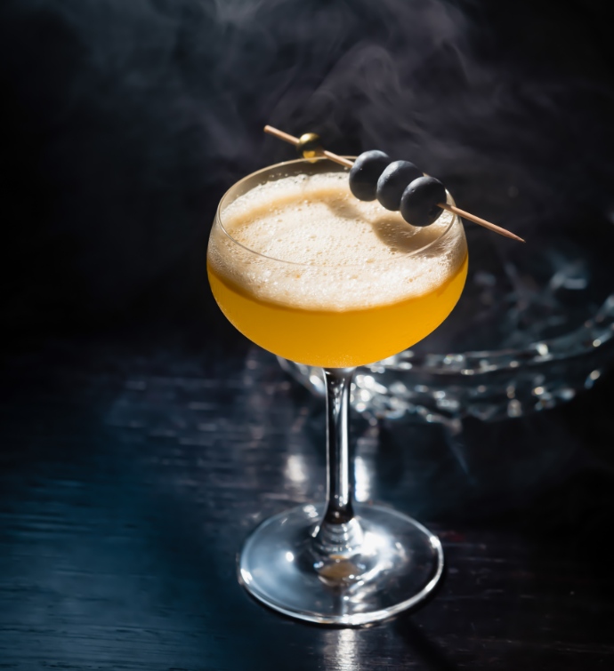 Yellow cocktail with blueberry garnish, with a crystal ash tray in the background