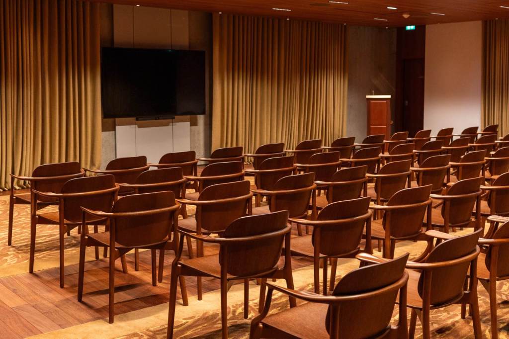 Empty chairs arranged in rows in a room facing a screen surrounded by curtains