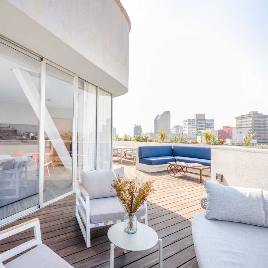 Rooftop terrace with lounge seating, coffee table with plant, and cityscape in the background