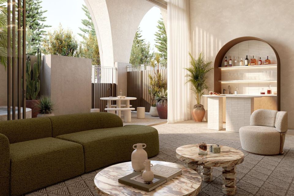 A living area with a modern dark green couch, two marbled coffee tables, a small cream chair, and plants decorating the space