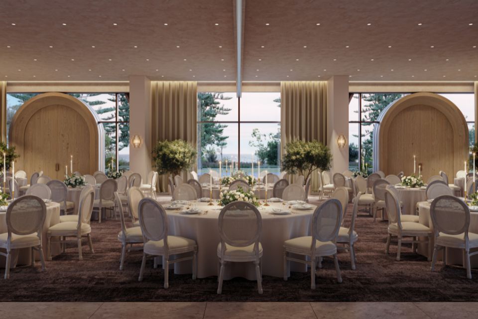 Ball room with large circular tables and chairs, large candlesticks and flowers on tables, and large windows in the background