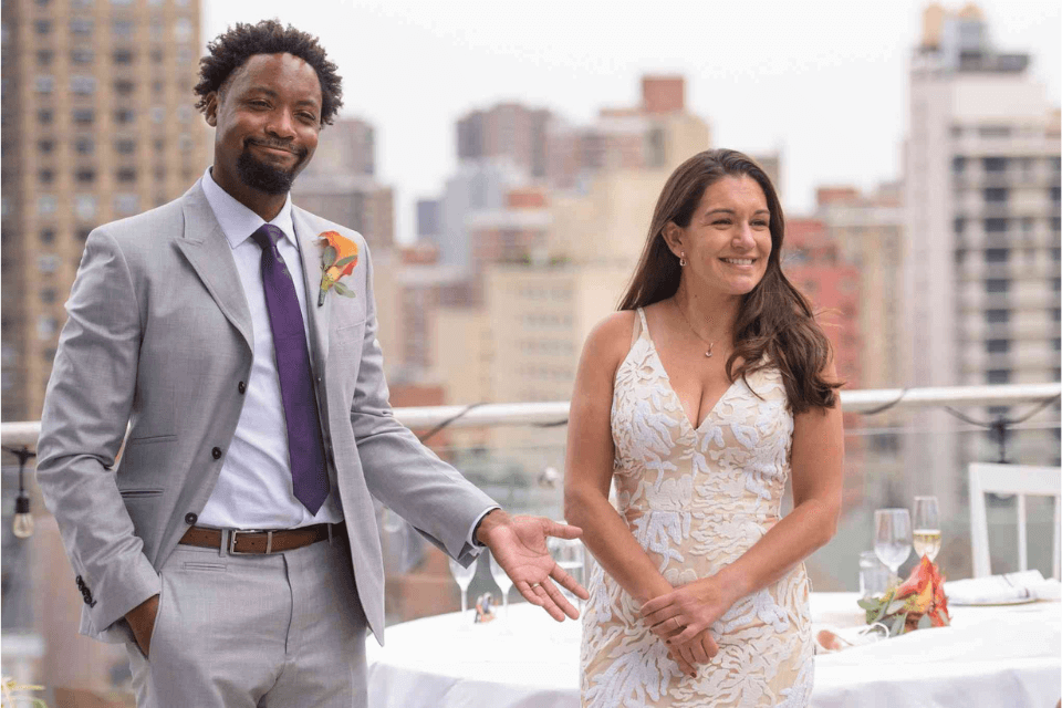 Bride and groom stand on a roof top with the city scape behind them