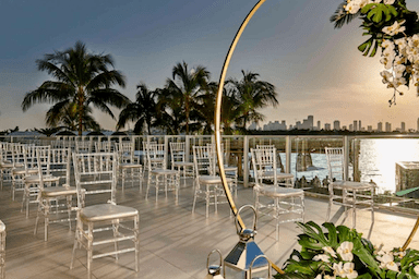 Rows of silver chairs set up on an outdoor patio during sunset with palm trees in the background