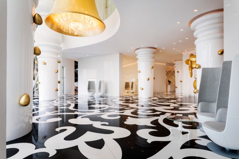 Large lobby with black and white intricate tile, large white columns, and gold wall decorations