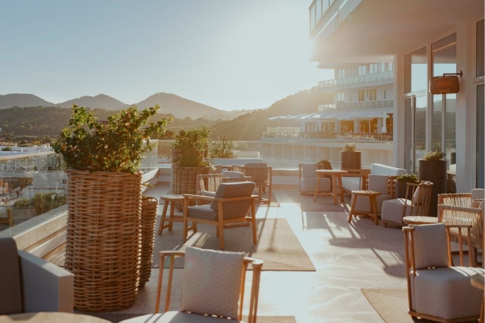 Sun shining over a large patio with outdoor chairs, plants, and more furniture looking out to mountains