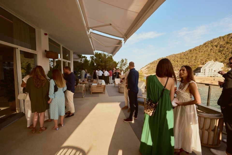 Group of people in cocktail attire gathering on a balcony overlooking the sea