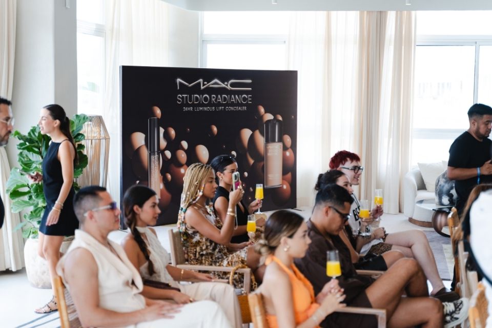 Group of people sitting in rows of chairs with large printed MAC advertisement in the background