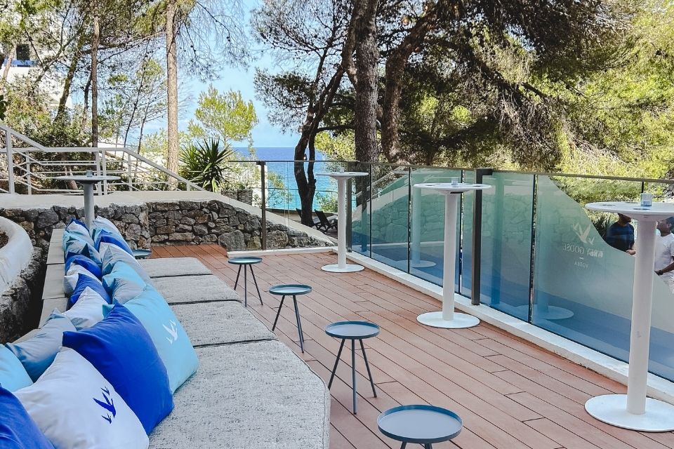 Outdoor patio with large grey sofa and grey goose branded pillows with small blue tables scattered