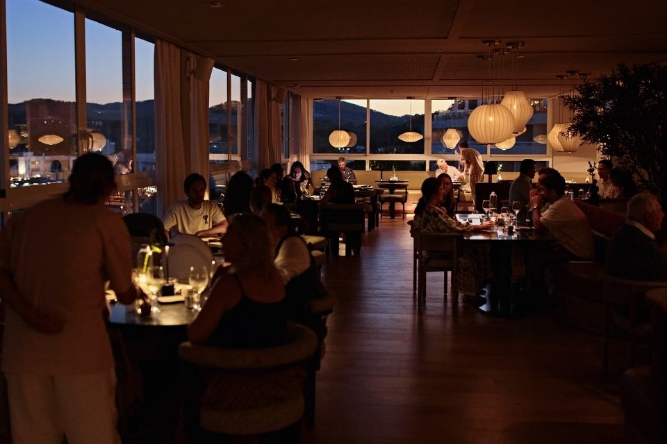 Evening with soft light in a large dining room filled with people at tables