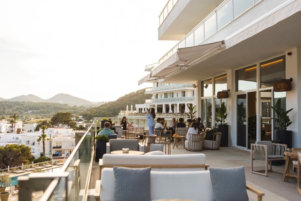 Large outdoor patio with outdoor sofas, chairs, and people gathering together with mountains in the background