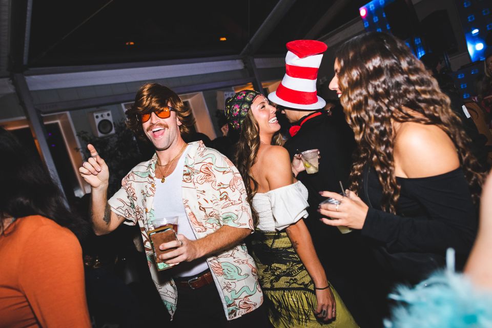 Man in 70s style costume dances with other people in costumes in the background