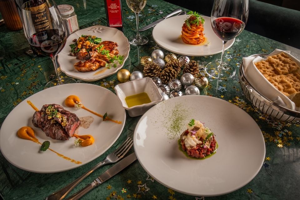 Four white dishes with meats, vegetables, and pasta on a green table decorated with acorns and festive items