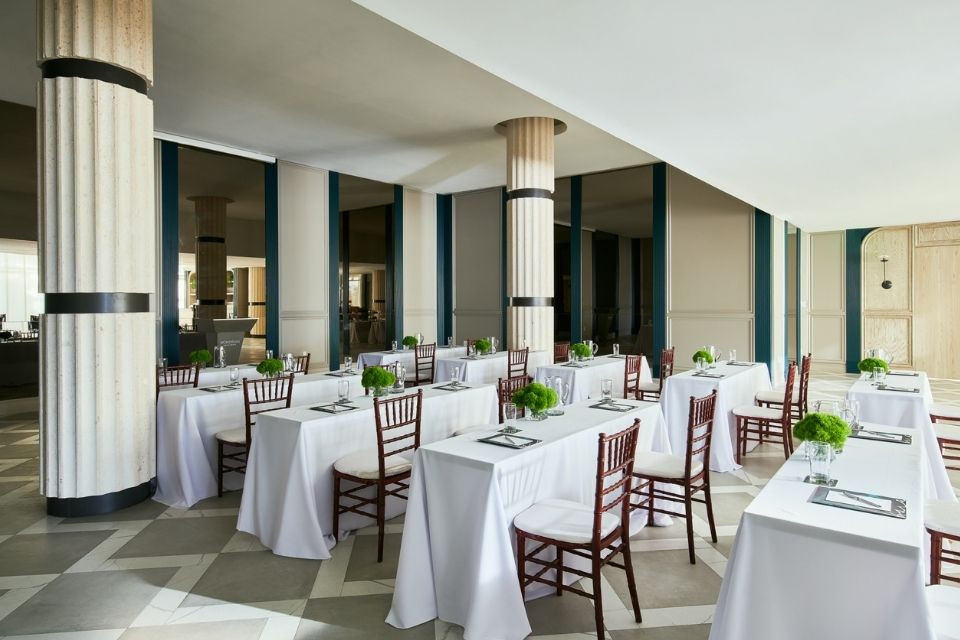 Banquet set up with rows of white tableclothed tables and wooden chairs decorated with notepads and floral arrangements on top