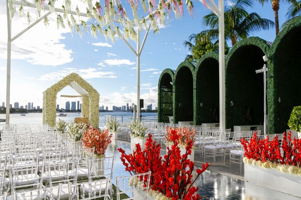 Outdoor wedding ceremony set up with rows of chairs, flowers, and beach in the background