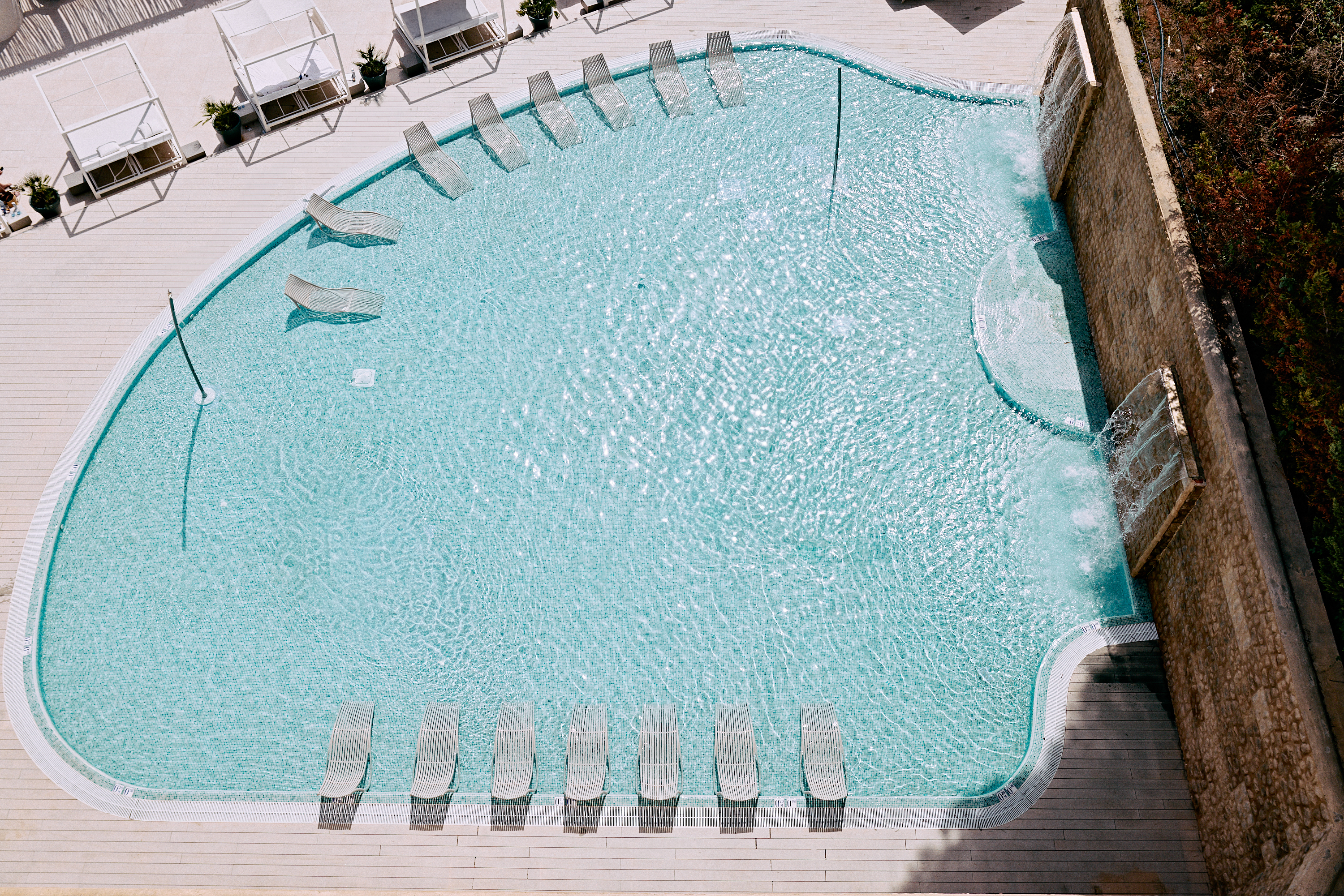 Hyde Ibiza Wet Deck Pool with white sun loungers and bali beds. The pool area includes a waterfall.