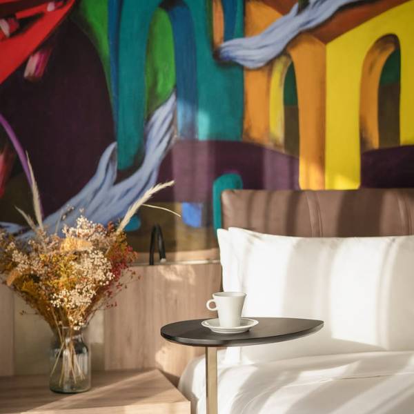 White hotel bed with colorful wall and side table with coffee cup on top