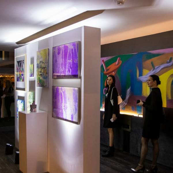 Art gallery in dark-lit space with two women wearing black looking at art